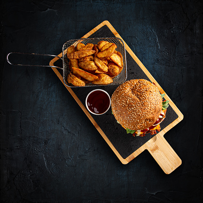 Tasty burger and golden potatoes with bbq sauce on dark background