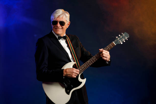 istock Musician Guitarist Active senior Handsome man playing guitar. Blue  background, with rays of light and special effects smoke. 1224764795