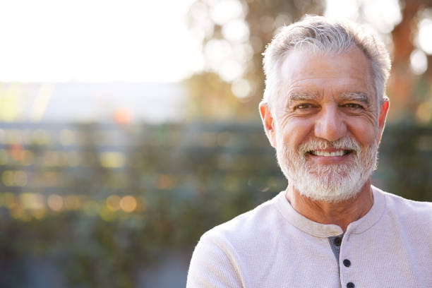 портрет улыбаясь пенсионеров старший испаноязычный человек в саду у себя дома против сжигания солнца - senior male стоковые фото и изображения