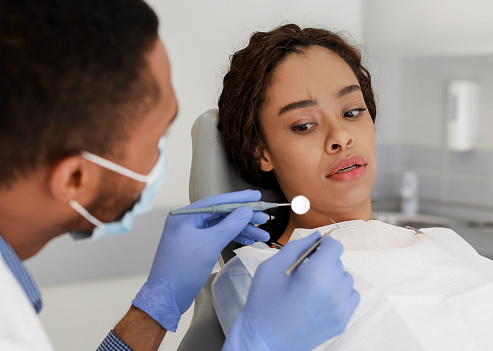 Mujer negra asustada mirando herramientas dentales en manos de médico photo