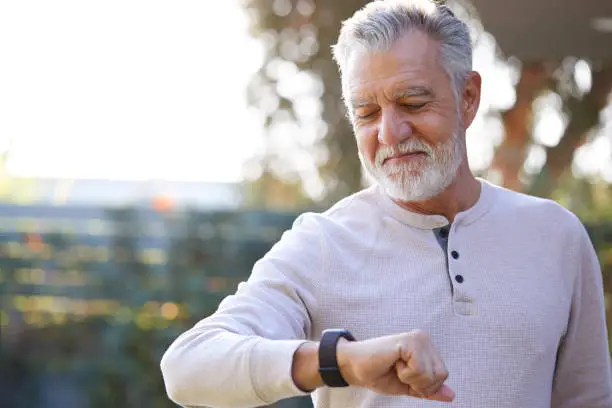 Senior Hispanic Man Checking Health Monitor On Smart Watch In Garden At Home