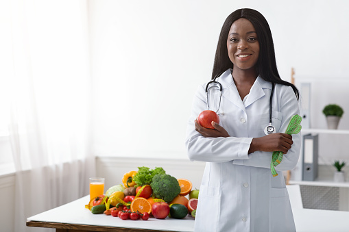 Friendly black woman dietician with apple and tape recommending fruits and vegetables during quarantine, copy space