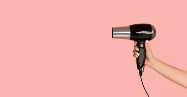 Unrecognizable girl showing hairdryer on pink background, copy space. Panorama