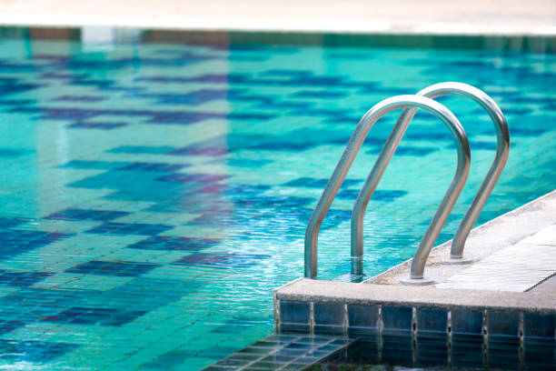 Outdoor swimming pool with blue water during nobody use. Selective focus at the ladder's handrail.