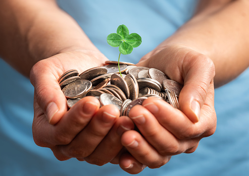 Woman holding money with small four leaves clover growing from it