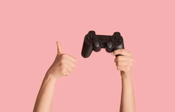Stay home hobbies. Millennial girl showing video game joystick and thumb up gesture on pink background, closeup