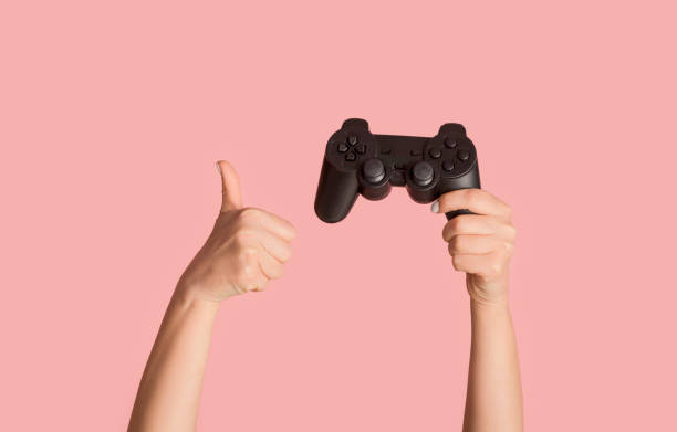 fique em casa hobbies. garota millennial mostrando joystick de videogame e gesto de polegar para cima no fundo rosa, close-up - hand games - fotografias e filmes do acervo