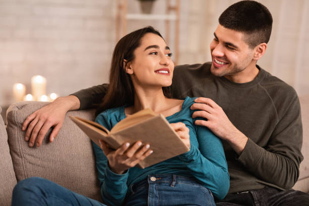 istock Lovely couple sitting on couch reading book together 1224771530