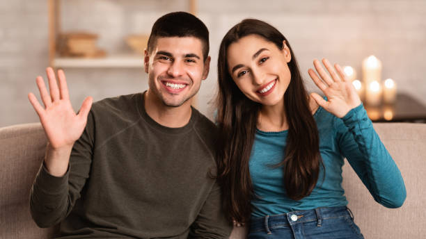 istock Couple sitting on sofa at home and waving to camera 1224772760