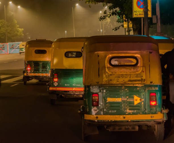 Three wheeled CNG powered Iconic auto rickshaws of India plying on the roads of Delhi downtown during late night commute of foggy Winter nights. - Image. Photo of Three Autorickshaws plying on Delhi roads during the late night hours for commuters who work till late. Such autos are iconic for travelling in Delhi, is generally three wheeler and can accommodate 03 persons including the driver, and can be taken from taxi stands and they run on meter. The autos are for hire and have comparatively low fares and use CNG as fuel thus promoting the clean renewable energy as means of transport for commercial vehicles. auto rickshaw taxi india stock pictures, royalty-free photos & images