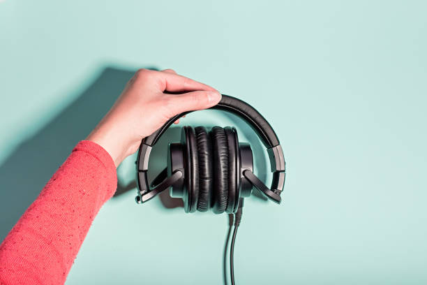 istock Woman holding black overhead headphones on blue background, copy space. Modern technology flat lay with over-ear earphones and cable, modern lifestyle gadget concept 1224780899