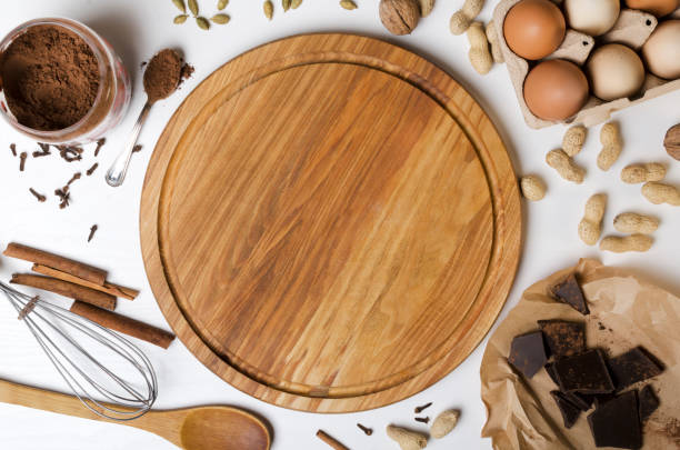 istock Top view of wooden cutting board adn ingredients for baking.Chocolate, peanuts, eggs, cocoa, cinnamon, cardamon, kitchen utencils on the white table.Empty space 1224780939