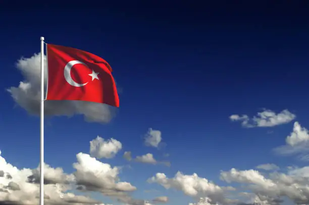 Turkish flag on a flag pole and blue cloudy sky. Turkish flag is with a crescent and a star shape on a red background.