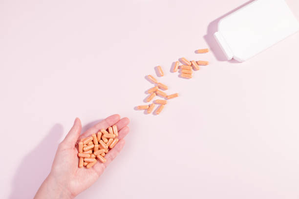 mulher tomando vitaminas e suplementos. cápsulas de vitamina laranja ou pílulas na mão feminina derramando de garrafa branca. estilo de vida saudável, vista superior, fundo pastel - capsule pill lecithin fish oil - fotografias e filmes do acervo