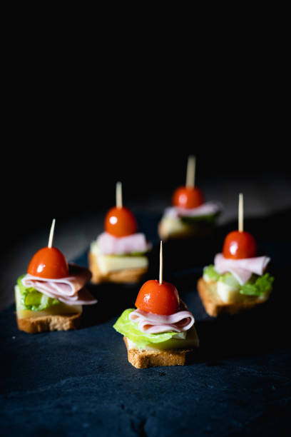 świeże przekąski z tostami, sałatą, szynką i pomidorem wiśniowym na kamiennej desce z ciemnym tłem - cherry tomato flash zdjęcia i obrazy z banku zdjęć