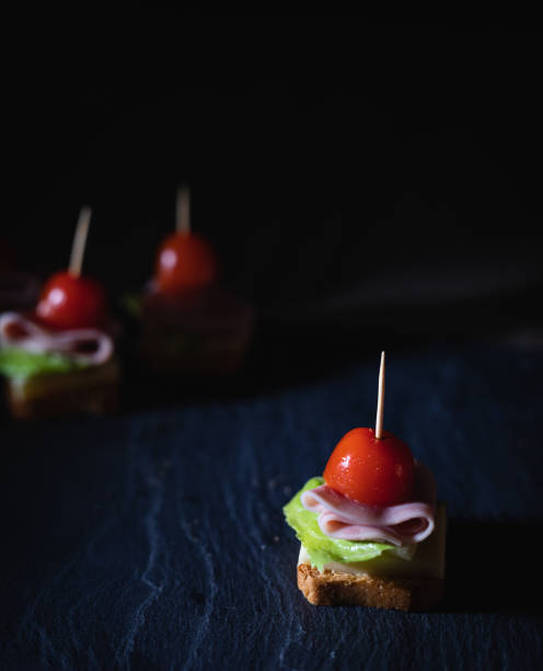 świeże przekąski z tostami, sałatą, szynką i pomidorem wiśniowym na kamiennej desce z ciemnym tłem - cherry tomato flash zdjęcia i obrazy z banku zdjęć