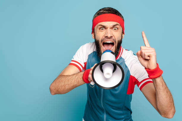 emotional stylish sportsman yelling in loudspeaker on blue background emotional stylish sportsman yelling in loudspeaker on blue background sweat band stock pictures, royalty-free photos & images