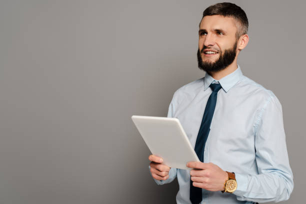 istock smiling handsome bearded businessman with digital tablet on grey background 1224785304