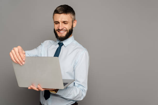 istock smiling handsome bearded businessman with laptop on grey background 1224785308