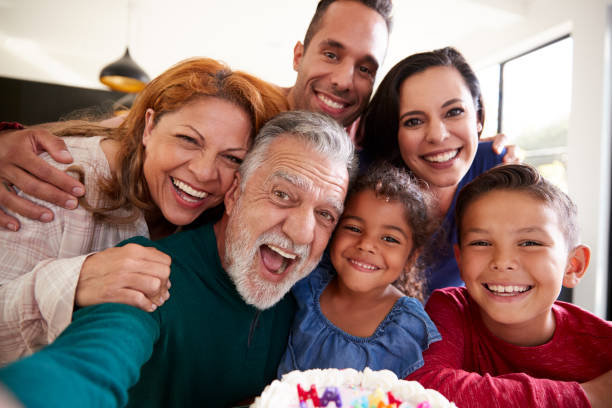 multi-generation hispanic family taking selfie to celebrate granddaughters birthday at home - wireless technology cheerful granddaughter grandmother imagens e fotografias de stock