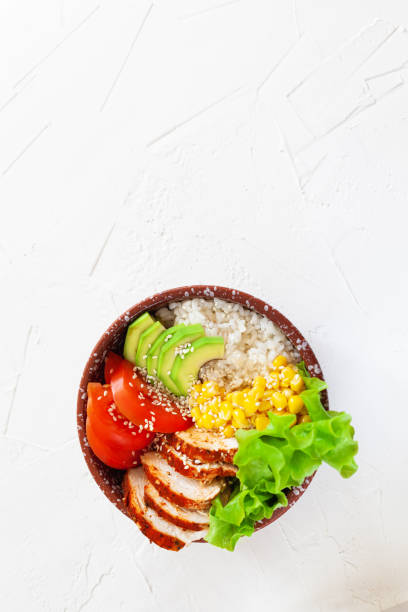istock Buddha bowl with rice, tomatoes, corn, chicken and avocado on a white table 1224787663