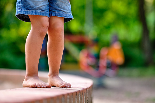 Low section of a 3 year old caucasian child girl in jeans shorts who is standing barefoot on a little stone wall with sandy feet in summer. Seen in Germany in August.