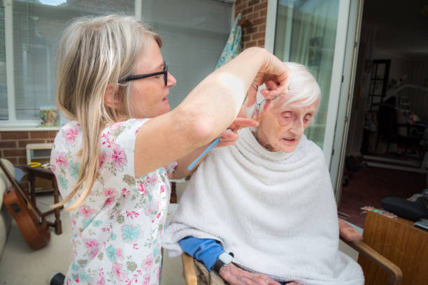 高齢の女性は、自宅でコロナウイルスのロックダウン中に彼女の介護者によって髪をカットされています。 - housebound ストックフォトと画像