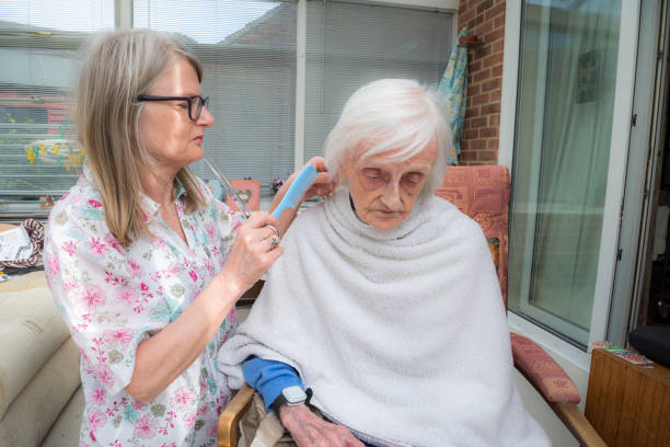 �高齢の女性は、自宅でコロナウイルスのロックダウン中に彼女の介護者によって髪をカットされています。 - housebound ストックフォトと画像
