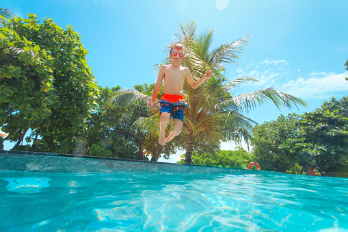 Happy boy jumping into swimming pool, kid on vacation, summer fun