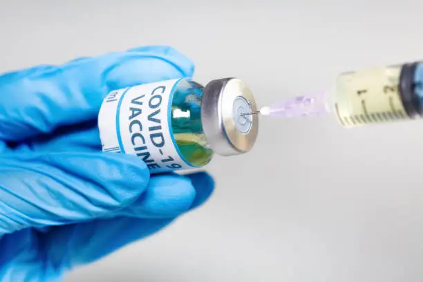 Doctor hand wearing medical gloves in close up view hold a vaccine bottle vial while transferring medication to an injection syringe used for treatment of Covid-19 patients