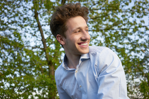 Portrait of a young handsome happily laughing man looking over his shoulder in beautiful greenery