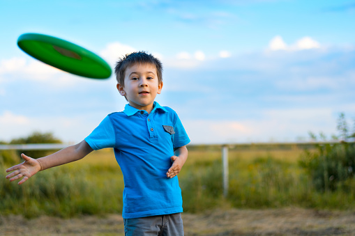 Boy playing with frisbee outdoors on sunset. Summer holidays concept