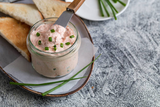 Salmon and soft creme cheese spread in jar. Salmon rillettes, mousse, pate and toasts on gray background stock photo