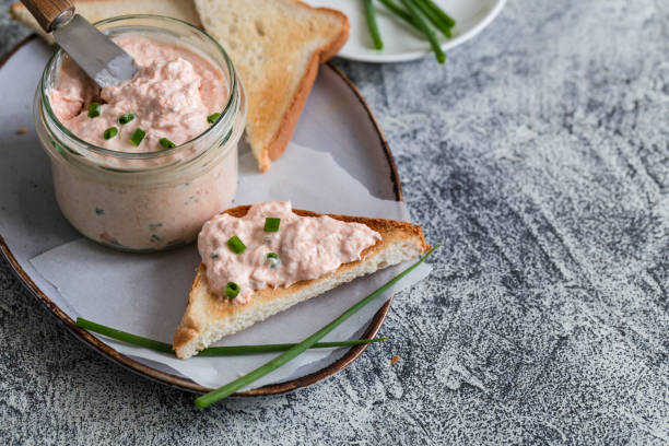 Salmon and soft creme cheese spread in jar. Salmon rillettes, mousse, pate and toasts on gray background Salmon and soft creme cheese spread in jar. Salmon rillettes, mousse, pate and toasts on gray background tuna pate stock pictures, royalty-free photos & images