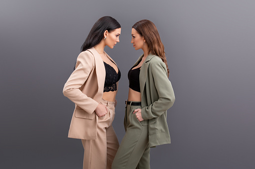 Fashion portrait of Two attractive business women wearing in suits and tops posing on grey background. quarrel, dispute, showdown