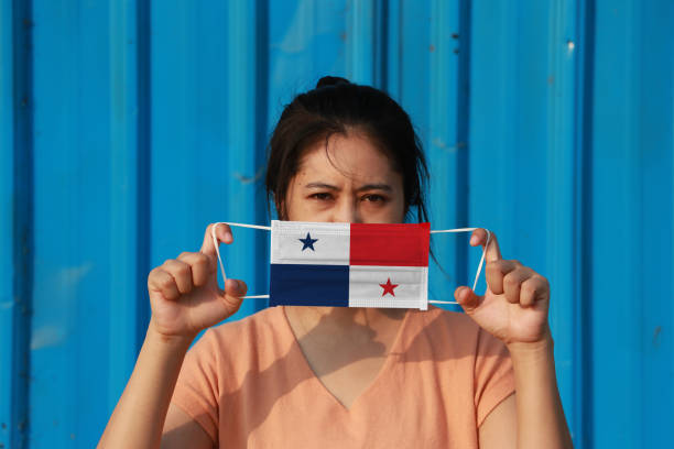 A woman with Panama flag on hygienic mask in her hand and lifted up the front face on blue background. Tiny Particle or virus corona or Covid 19 protection. stock photo