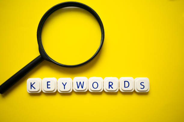 明るい黄色の背景の上に虫眼鏡と下の「キーワード」という単語。検索エンジンにおけるキーワードの重要性の概念。 - marketing internet customer searching ストックフォトと画像