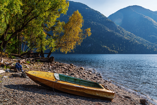 Old yellow metal boat on the shore of a mountain lake. Fall. Russia, Altai Republic, Lake Teletskoye