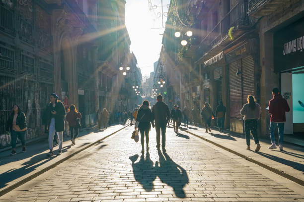 Barcelona, Spain - Jan 12 2020: Couple of people walk in middle of the road in the famous Gothic Square district with shopping bag under evening sunshine ray