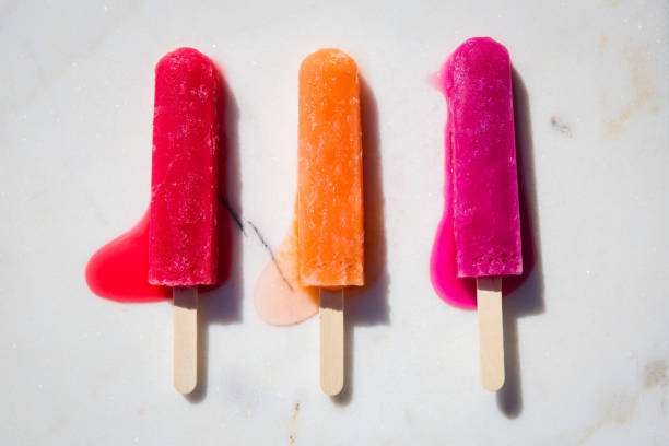 Red, orange, and pink popsicles melting on a white marble slab