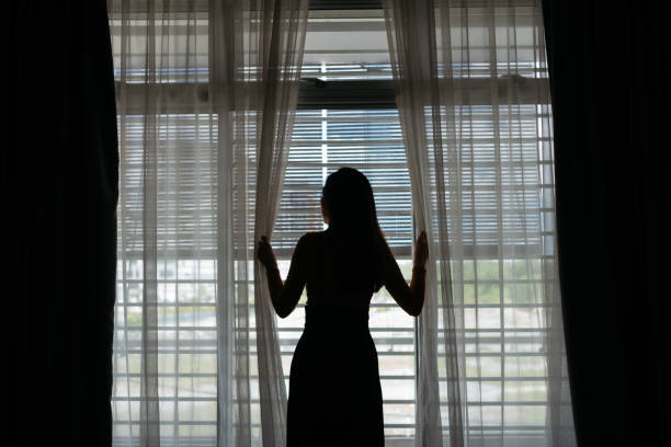 istock Young woman staying indoor and looking out from window 1224832190