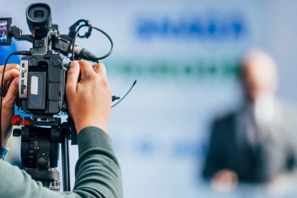 Press Conference Event. Cameraman Recording Male Speaker Cameraman recording well-dressed male speaker at press conference. Live streaming concept. microphone stand photos stock pictures, royalty-free photos & images