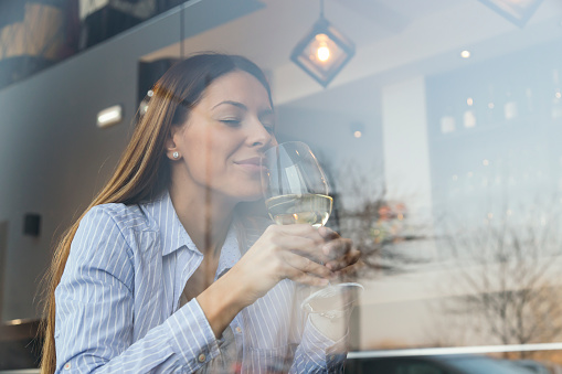 Beautiful young woman sitting at a restaurant table, drinking wine and enjoying her leisure time