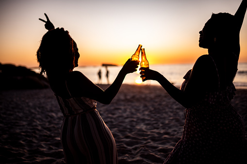 Two friends on the beach enjoying sunset while having a beer