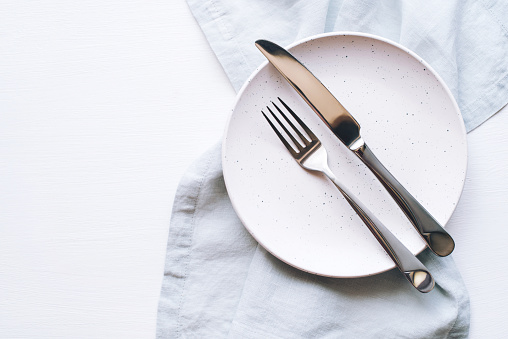 An empty plate and Cutlery on a white table. Top view.