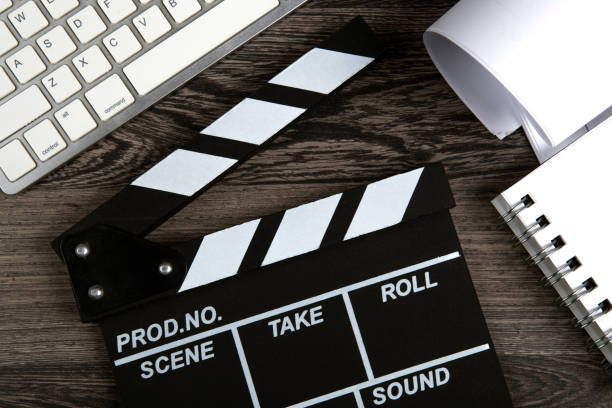 black movie clapper with keyboard and script sheets on a wooden table top view
