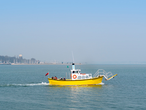 Passengers on the bright yellow harbour ferry which operates a triangular route between Shotley Gate in Suffolk, Harwich in Essex and Landguard Point in Felixstowe, Suffolk, Eastern England. In the background is the marina at Shotley Gate and the mouth of the River Orwell.