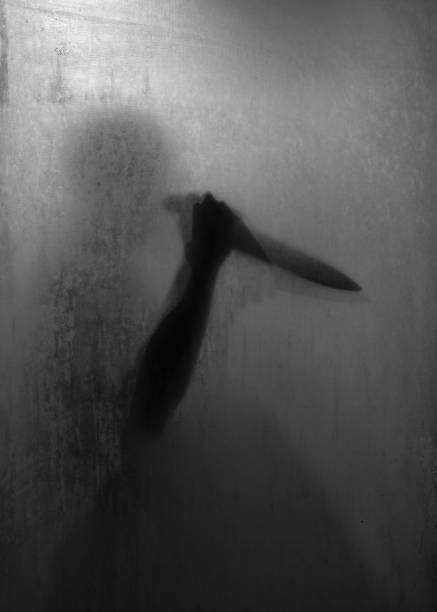 Shadow of horror murderer holding sharp knife behind frosted glass in the bathroom