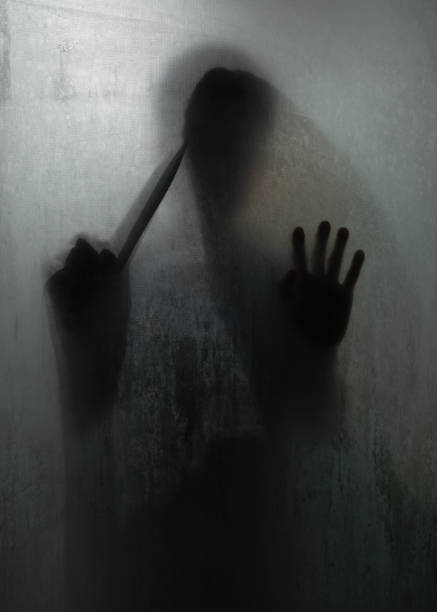 istock Shadow of horror murderer holding sharp knife behind frosted glass 1224857939