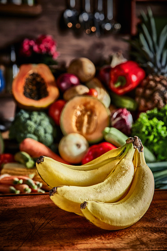 Assorted organic tropical fruits and vegetables in a rustic kitchen background.  Bell Red Peppers, carrots, lettuce, tomatoes, onions, celery, broccoli, carrots, cucumber, Zucchini, rucula, chieves, eggplant, papaya, bananas, pineapple, melon, corn.